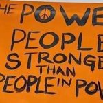 orange protest sign that says "the power of the people is stronger than the people in power"